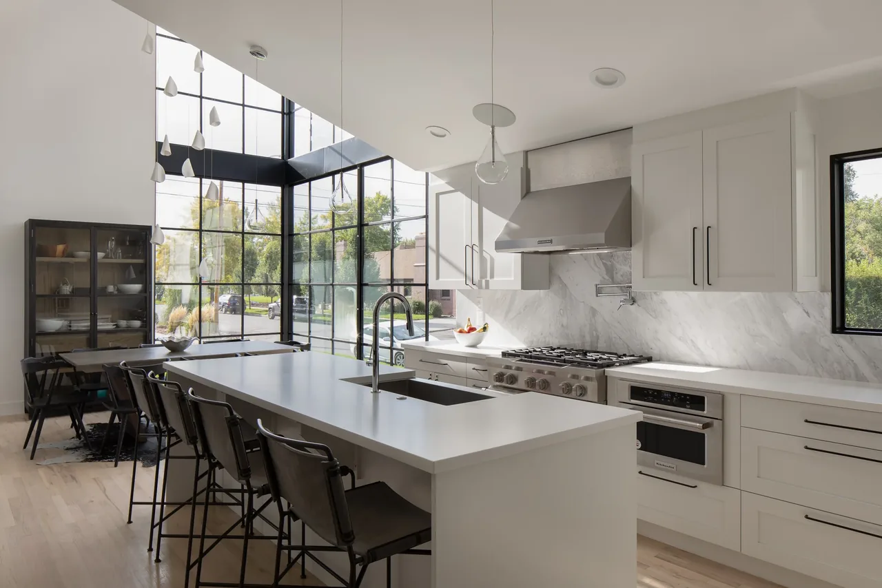 Modern kitchen featuring a large island with sink, gas range, and tall black-framed windows providing ample natural light.