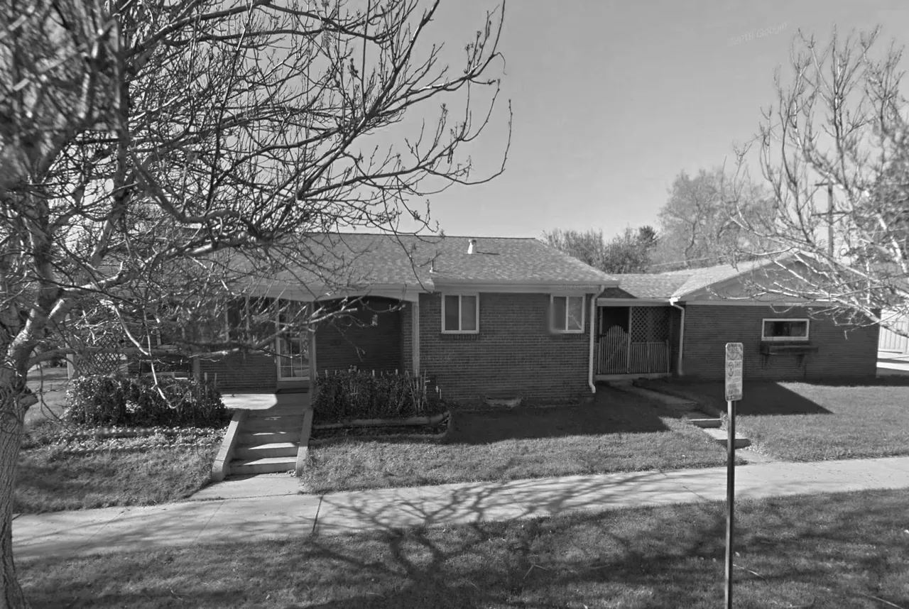 Single-story brick house with gable roof and symmetrical front windows, accessed by steps from the sidewalk.