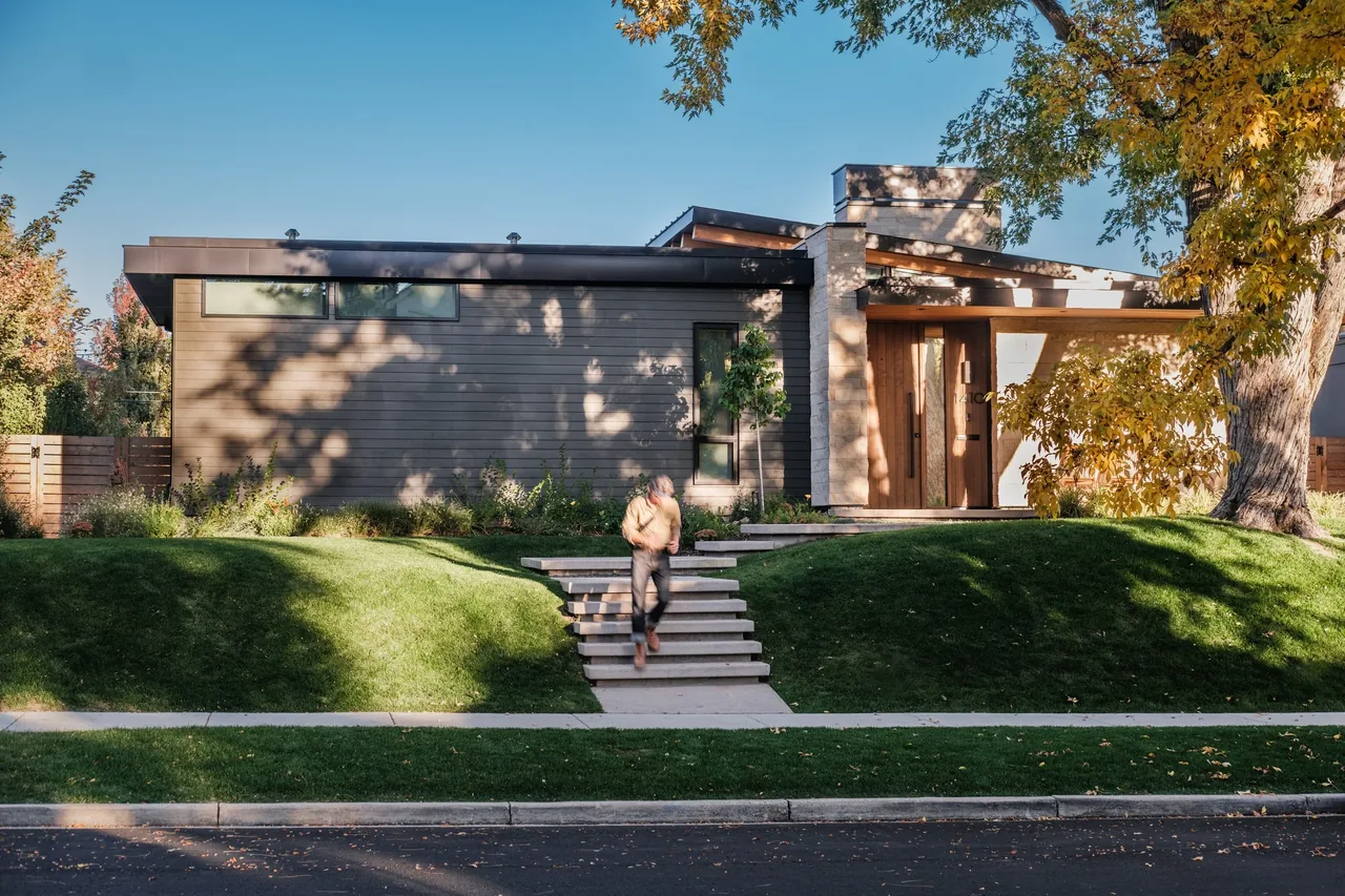 Front exterior of Wash Park Hideaway showing horizontal clerestory windows and illuminated entry with wood door and stone chimney.