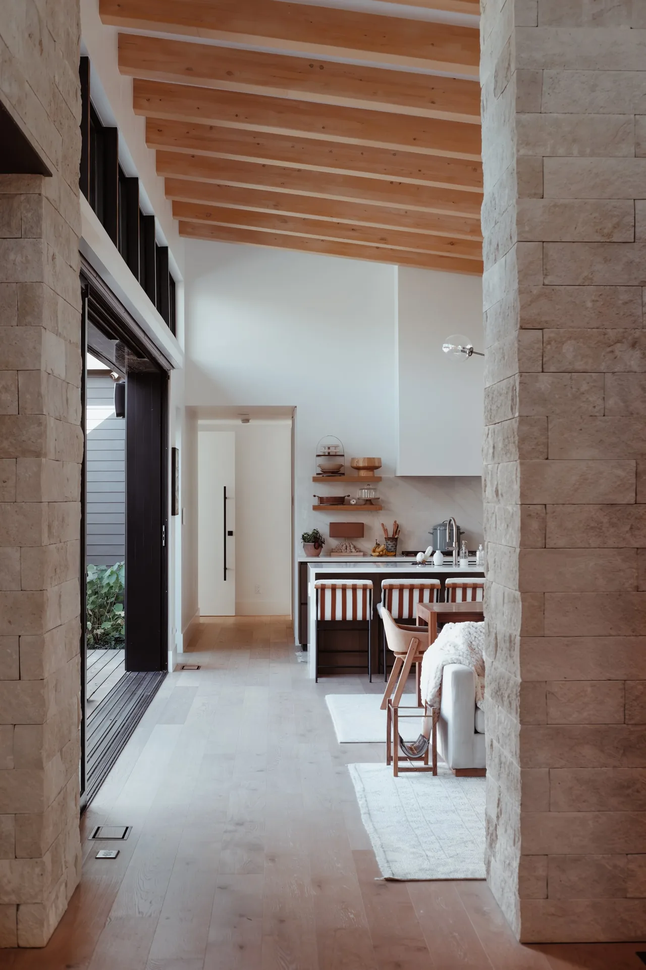 Modern kitchen and living space featuring light stone cladding and a wood beam ceiling