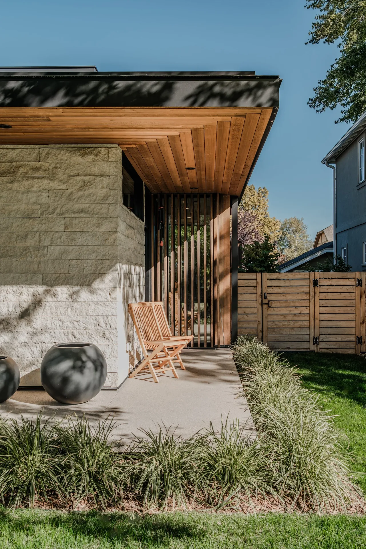 Outdoor seating area with wood ceiling, stone cladding, and a wood slat privacy screen.