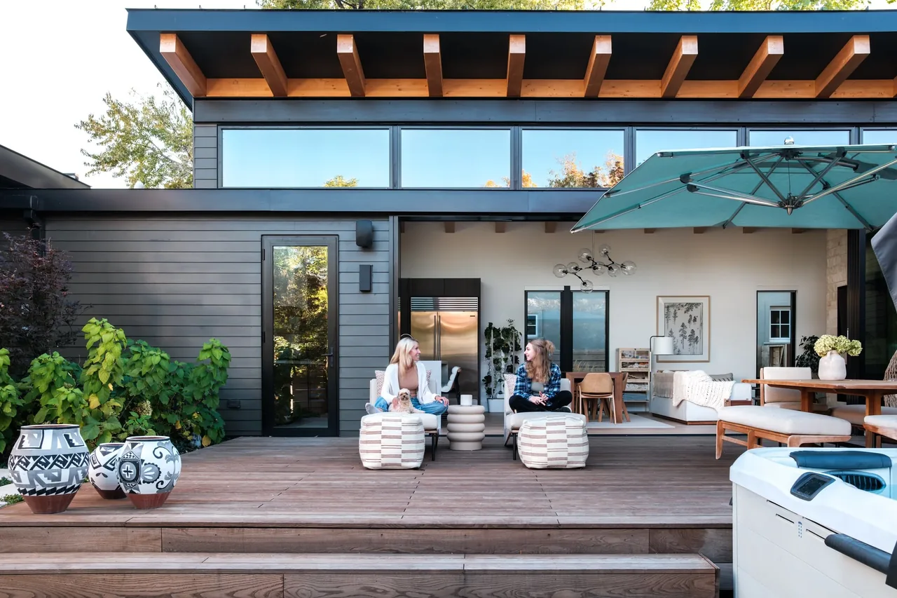 Modern house with wood deck, large glass doors, and a covered outdoor seating area with a blue umbrella.