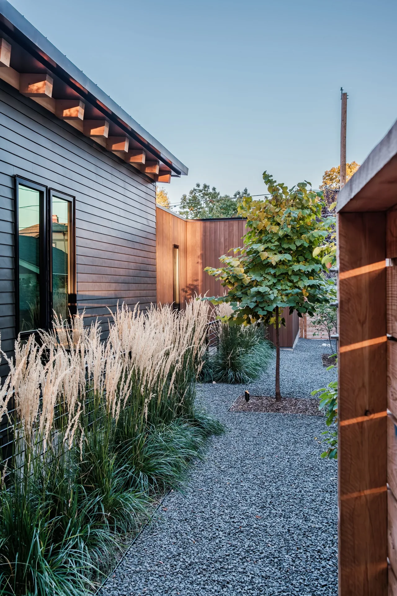 Modern exterior view showing black horizontal siding adjacent to vertical wood cladding with landscaped gravel path and plants.