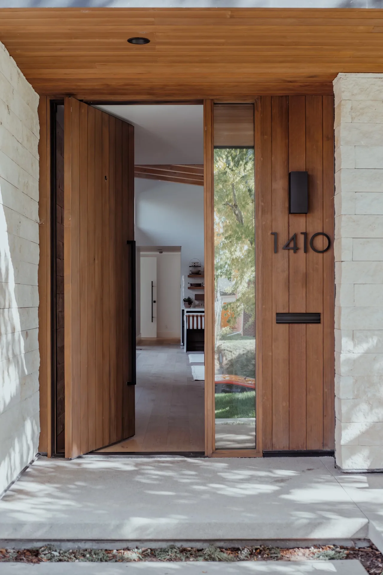 Entry of Wash Park Hideaway features a wooden pivot door, light stone walls, and integrated lighting.