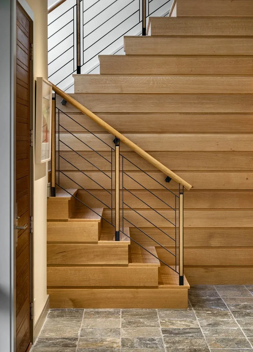 Interior wood staircase with black metal railing and stone tile flooring at Meadow Retreat.