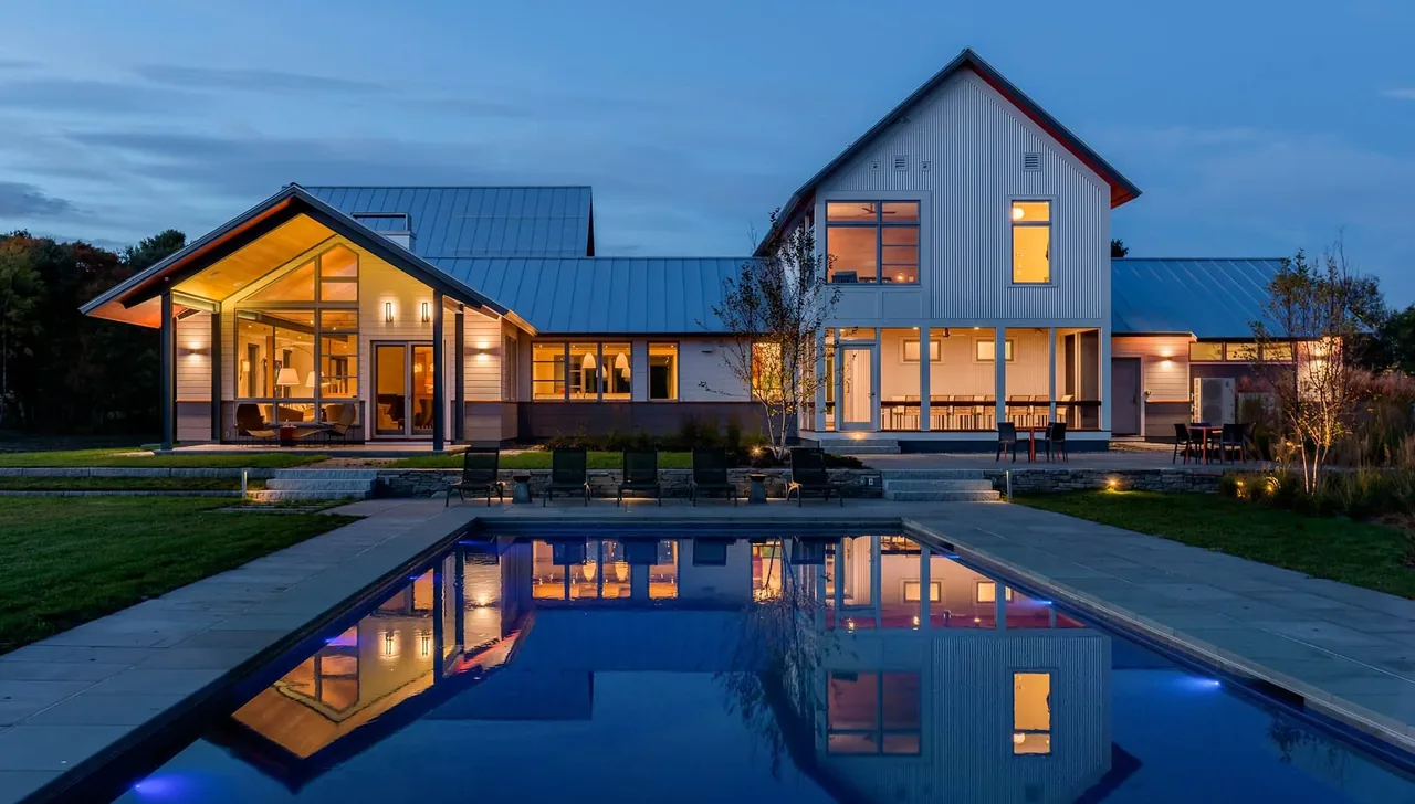 Meadow Retreat by Smith & Vansant Architects features metal roofing and a lit interior at dusk reflecting in a pool.