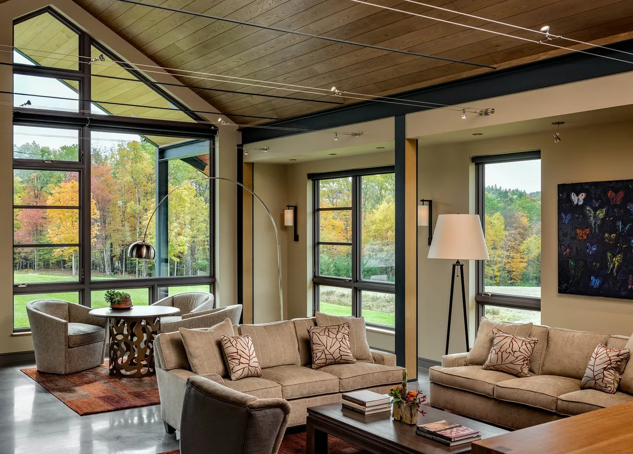 Living room of Meadow Retreat with large windows showcasing autumn foliage and modern furnishings.