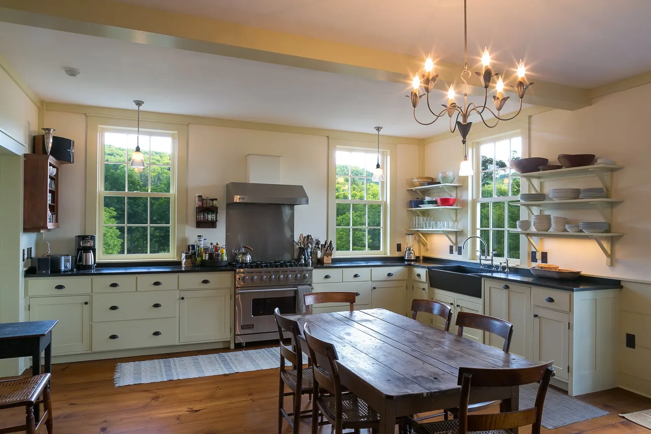 Kitchen of Corinth Retreat with white cabinets, black countertops, stainless steel range, and wooden dining table with chandelier.