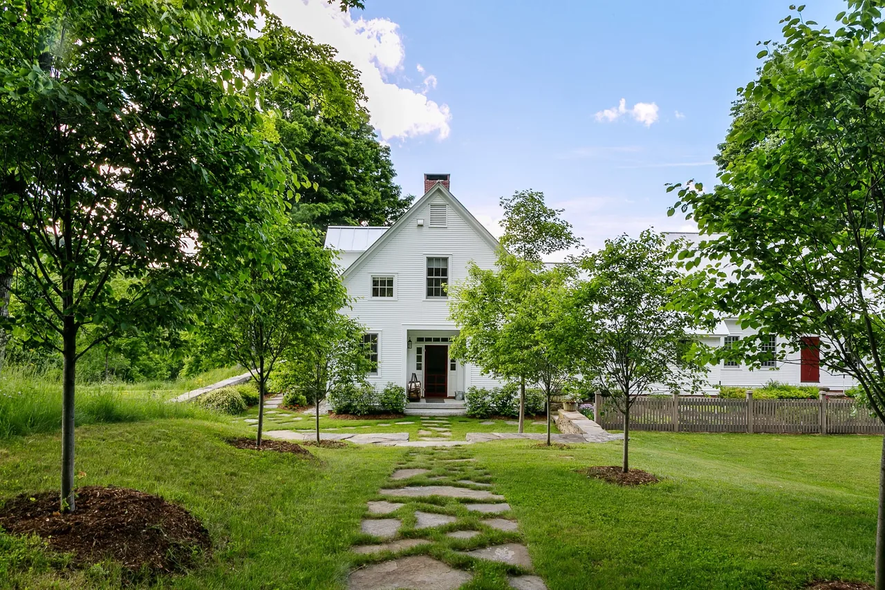 The Corinth Retreat features white wood siding, a gable roof, and a stone path through landscaped grounds.