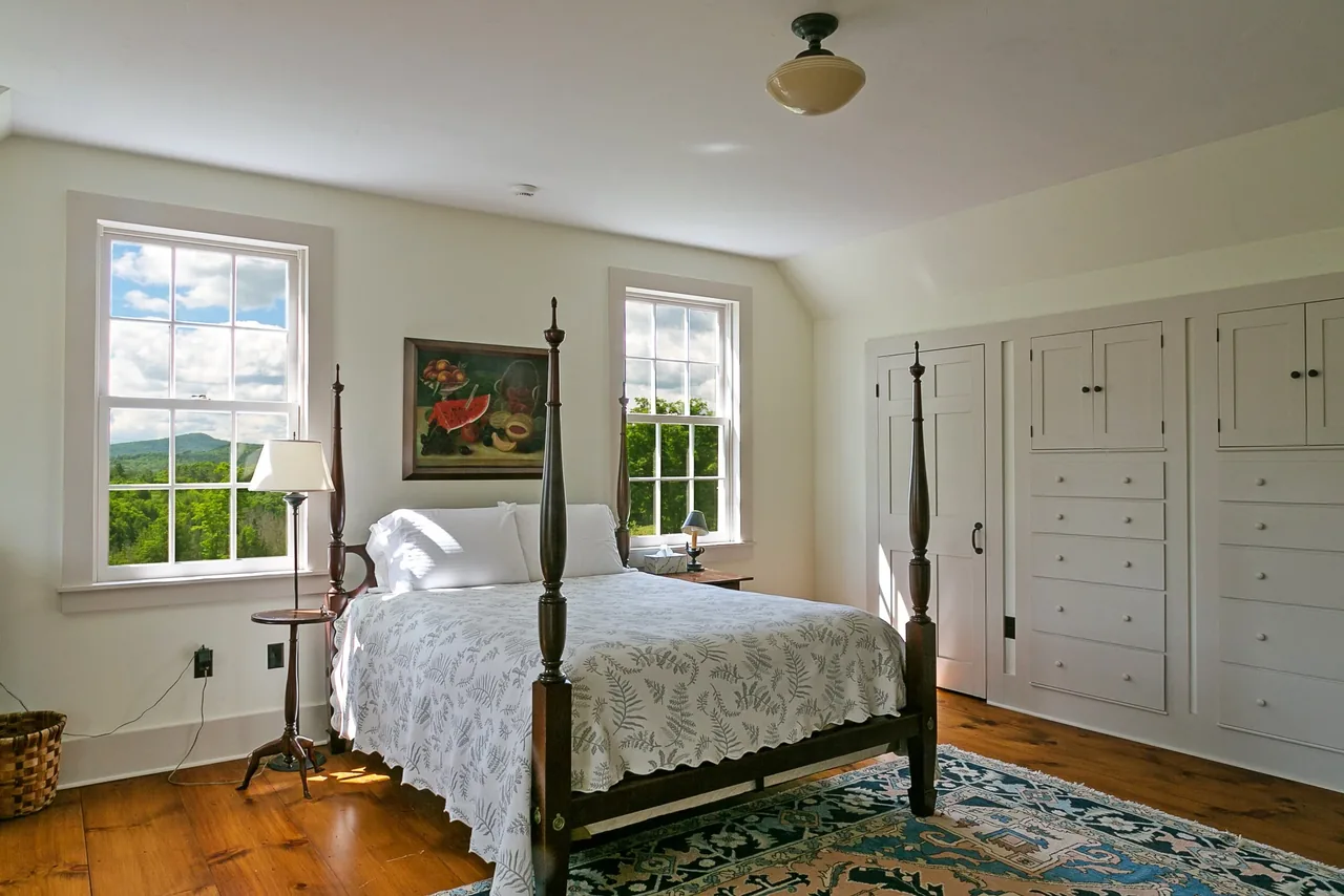 The Corinth Retreat bedroom features a dark wood four-poster bed, white built-in storage, and two large windows showing green landscape views.