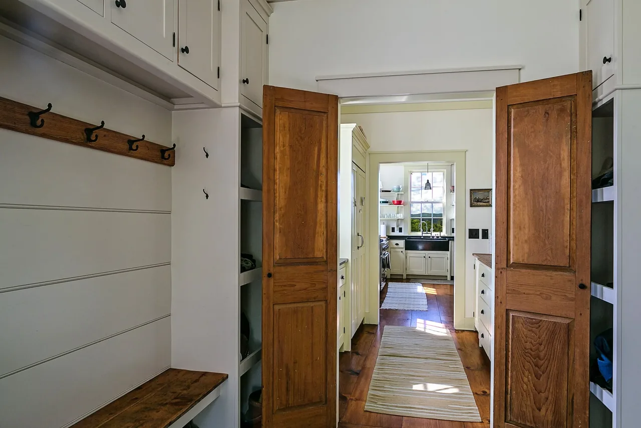 Interior view from hallway with wooden doors showing kitchen with black countertop and white cabinets.
