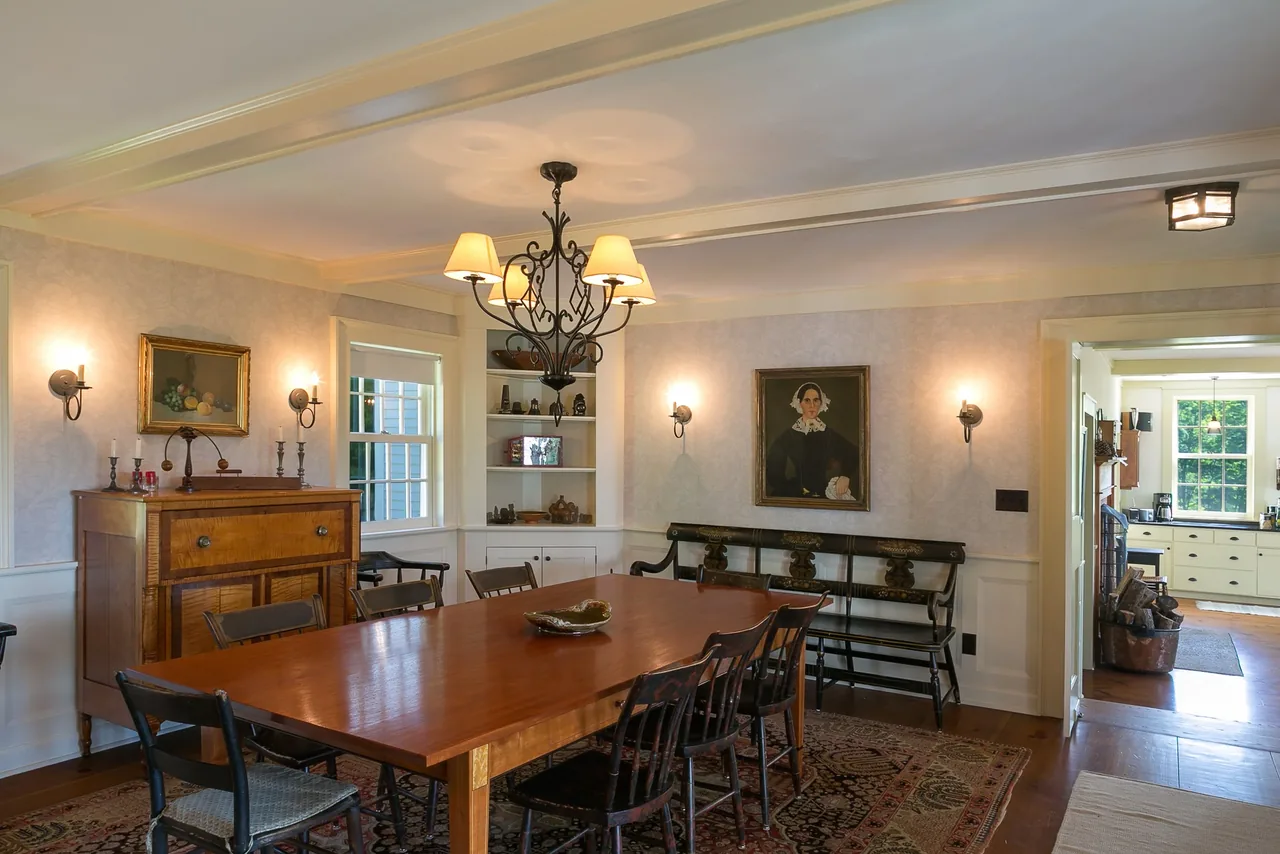 Dining room featuring a large wooden table, mixed chairs and bench seating, illuminated by a wrought iron chandelier and wall sconces.