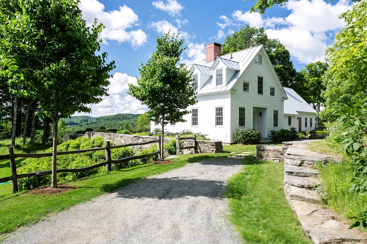 The Corinth Retreat features a white traditional house with a metal gable roof and stone wall landscaping.