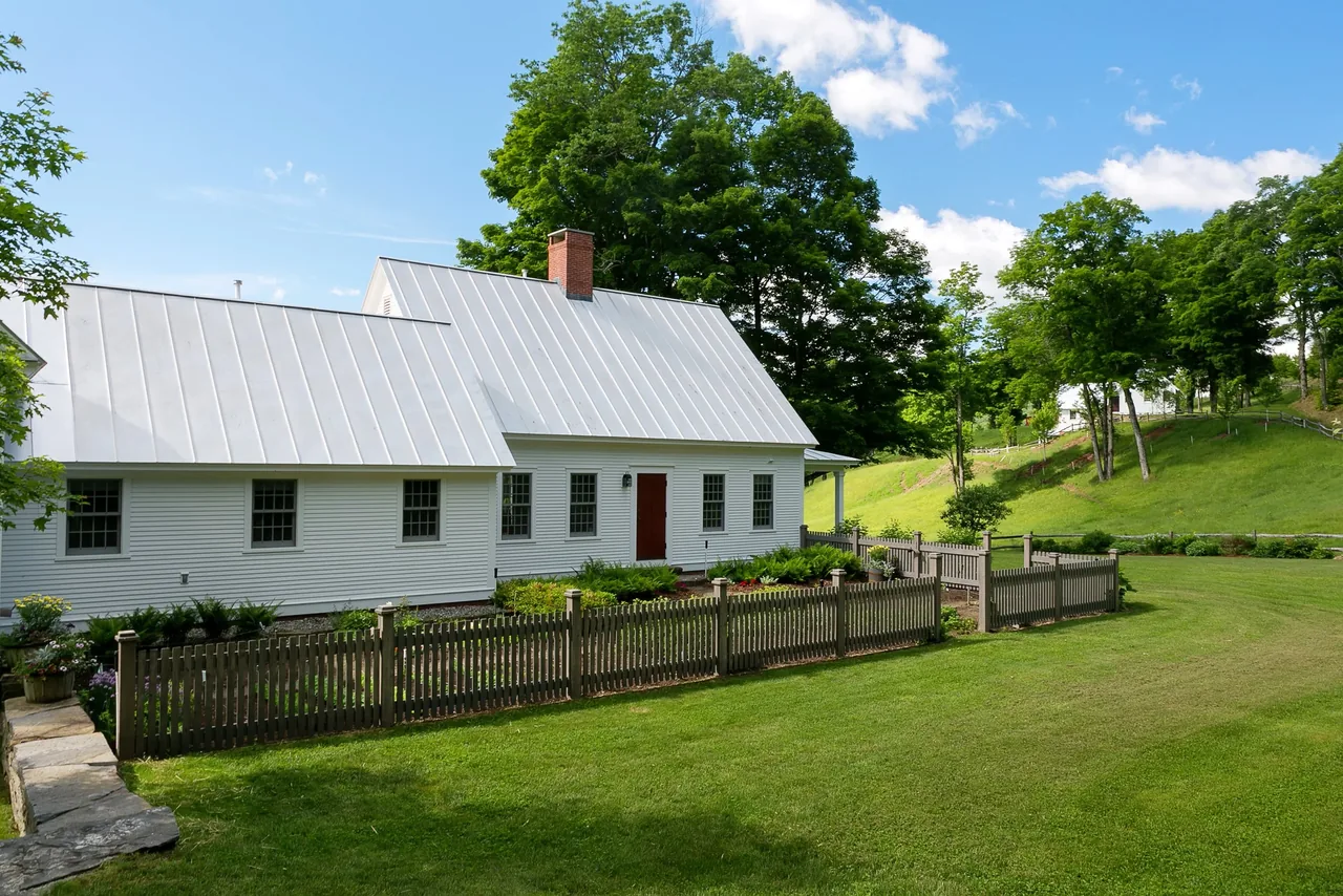 The Corinth Retreat features a white exterior with a metal roof and a wooden picket fence enclosing a small garden area.
