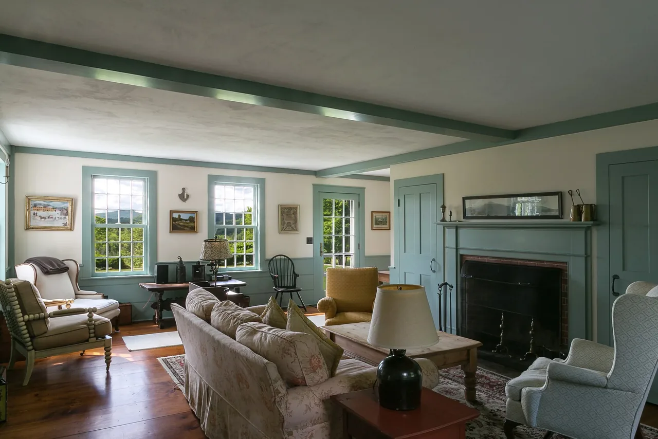 Living room of Corinth Retreat features vintage-style seating, a wood mantel fireplace, and light green window and door trim.