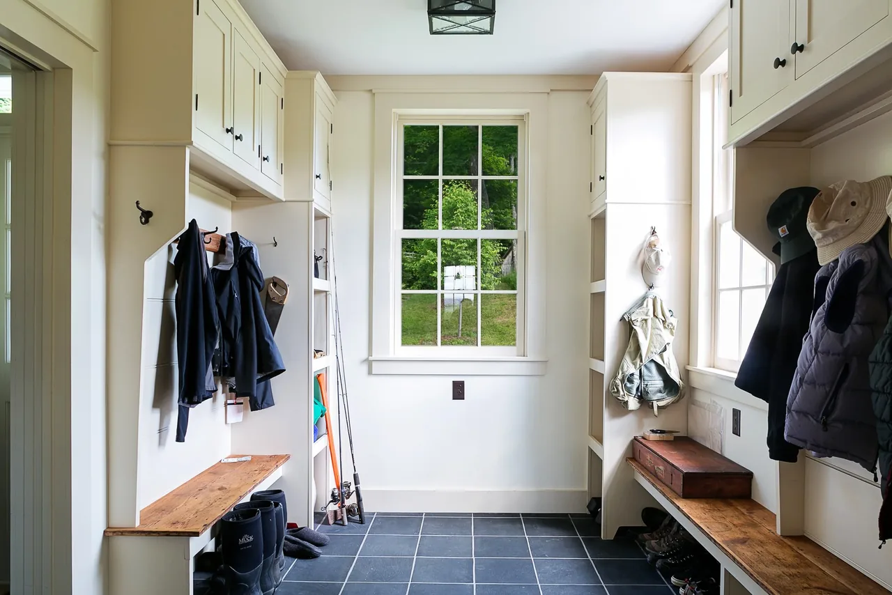 Mudroom featuring built-in white cabinets, wood benches, black tile floor, and a central window with divided lites.