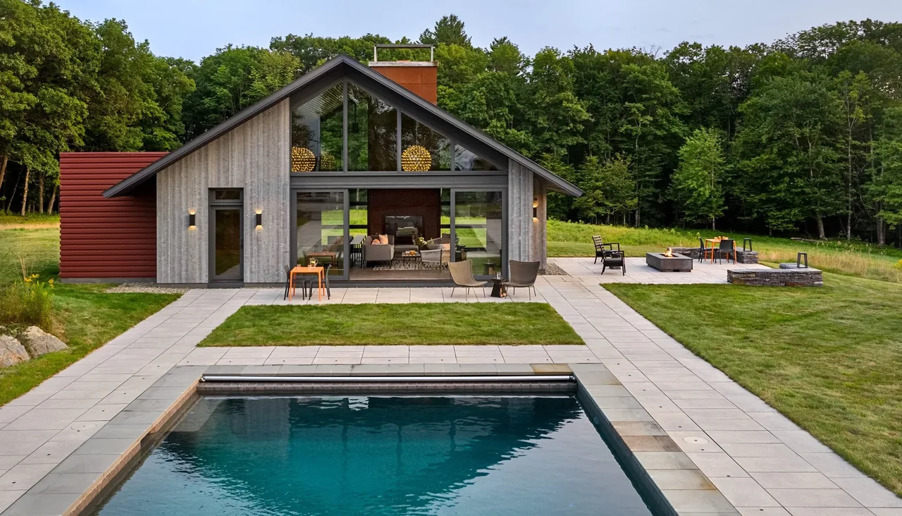 Exterior front of a modern lake retreat house with concrete pavers, a pool, and outdoor fire pit area.
