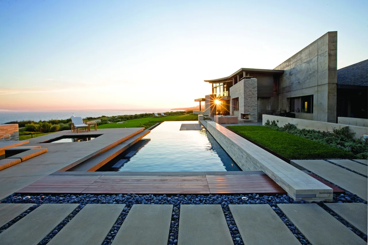 The Altamira project showcases an infinity pool beside a contemporary concrete home with an outdoor seating area at sunset.