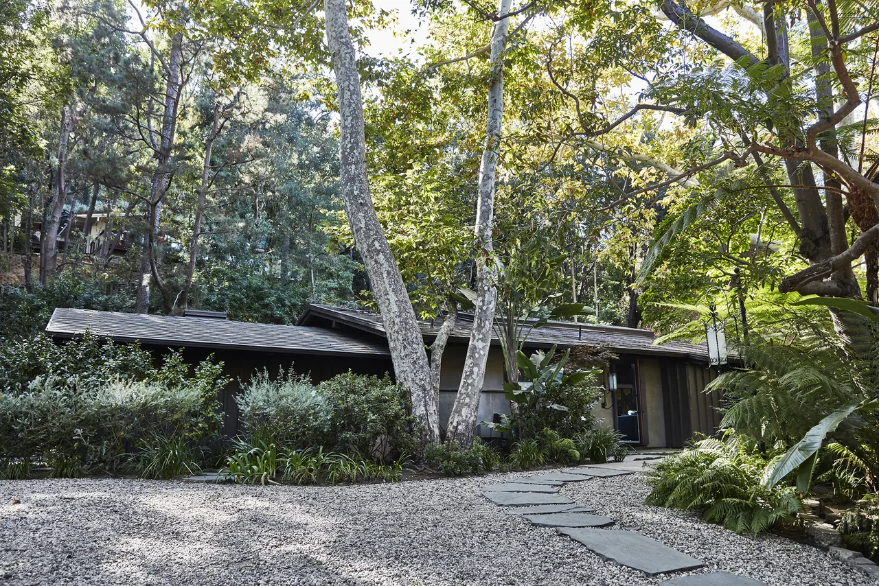 Experimental Ranch by Marmol Radziner Architecture features dark vertical siding and lush natural landscaping with stone pavers leading to the entry.
