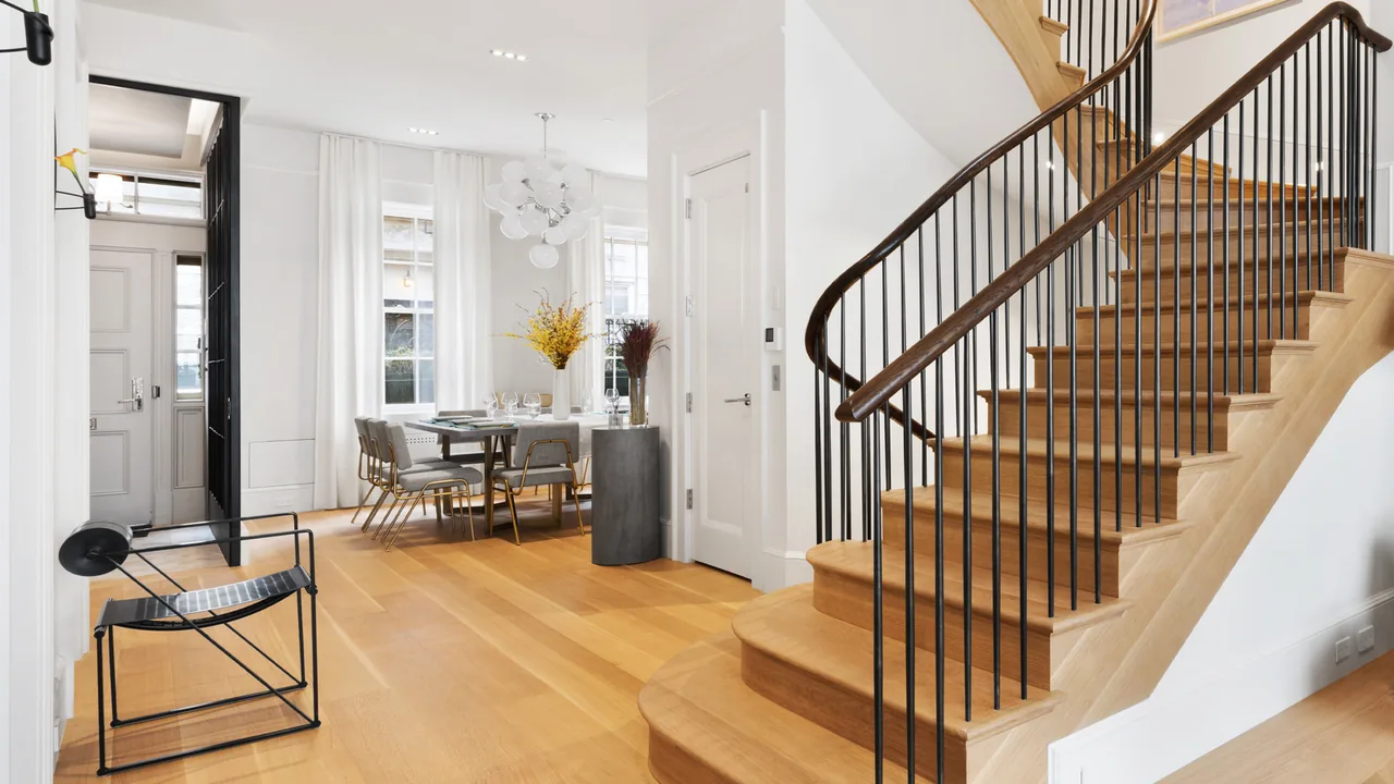 The West Village Townhouse interior features a light wood staircase with black metal balusters and a dining area illuminated by large windows.