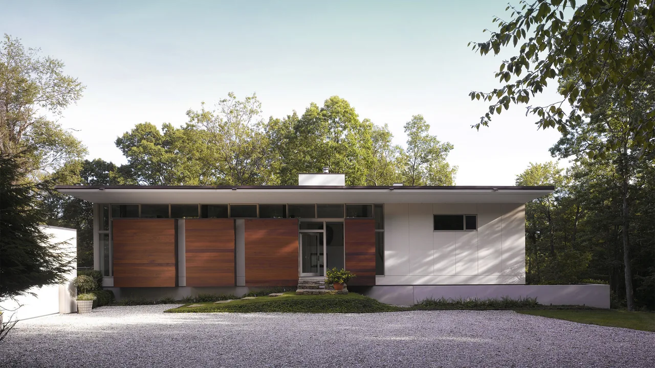 Pawling Residence features a flat roof with wood paneling and white exterior walls, nestled among trees in a natural landscape.