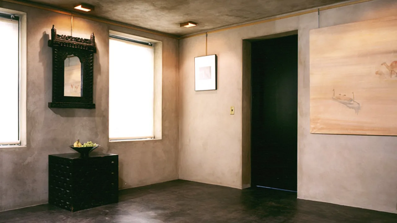 Artist's Townhouse room features plaster walls, small dark cabinet, and two covered windows providing soft light.
