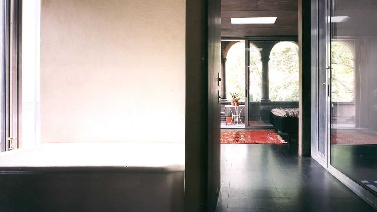 The hallway leads to a room with arched windows and a red carpet, featuring dark wood flooring and a skylight.