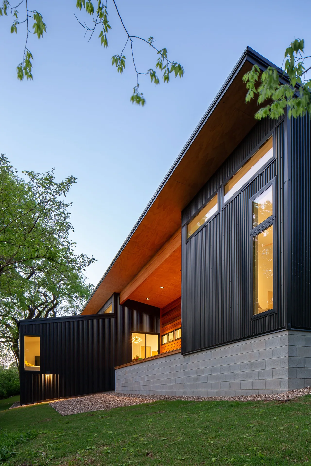 Modern house exterior with black metal siding, high windows, and a concrete block foundation under a sloped roof.