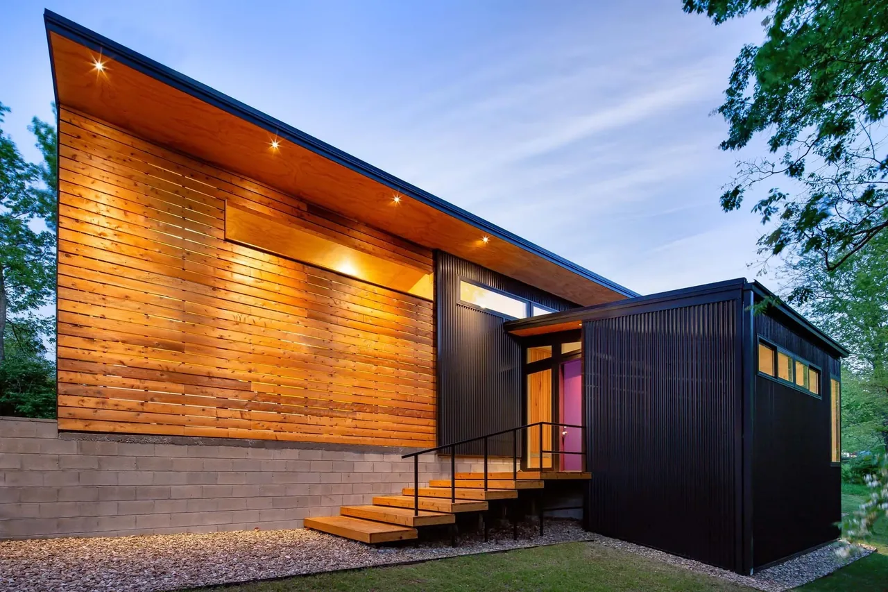 Modern exterior of a two-story house with wood cladding and black metal siding illuminated by recessed lighting.