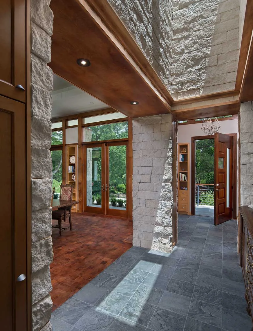 Entry hallway featuring rough stone walls, slate tile flooring, wood ceiling trim, and a skylight above.