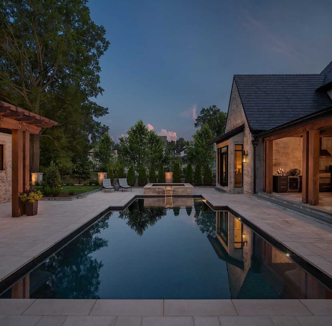 Evening view of a backyard with a rectangular pool and adjacent covered patio area.