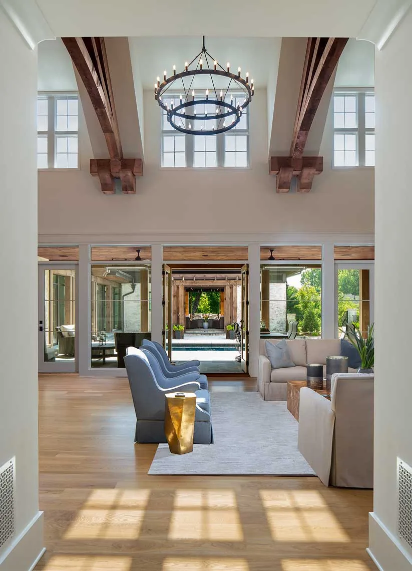 Haynes Bridge living room features vaulted ceiling with wood beams and circular chandelier overlooking a pool through glass doors.
