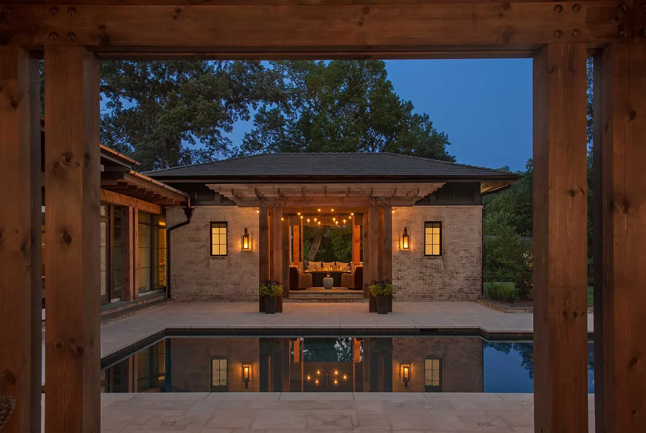 Covered outdoor living area with string lights next to a pool framed by wooden posts at dusk.