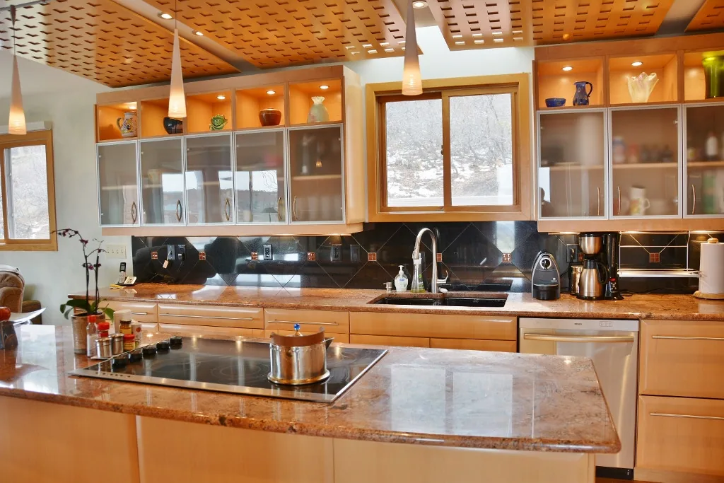 Kitchen features granite countertops, pendant lighting, and frosted glass upper cabinets in a modern style.