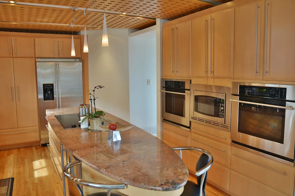 Kitchen with a granite island, stainless steel appliances, light wood cabinetry, and a patterned wooden ceiling.