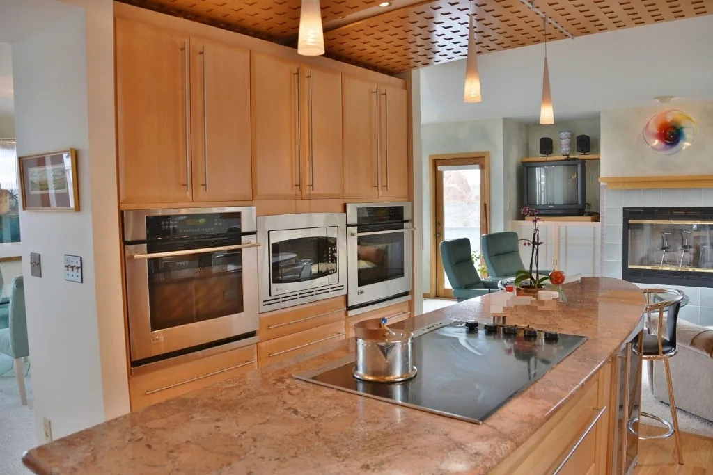 Kitchen featuring granite island with cooktop, wood cabinetry, double wall ovens, and a patterned ceiling.