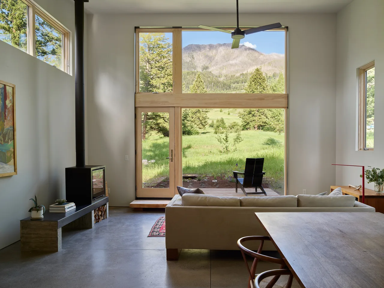 Living area of Willow Creek Ranch House with floor-to-ceiling windows framing mountain views and a small wood stove.
