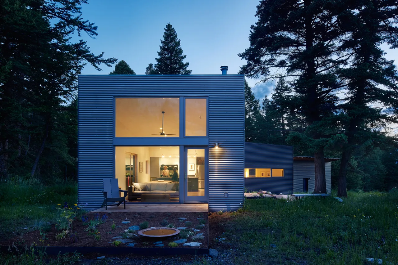 Willow Creek Ranch House features corrugated metal siding and expansive glazing in a forest setting at dusk.