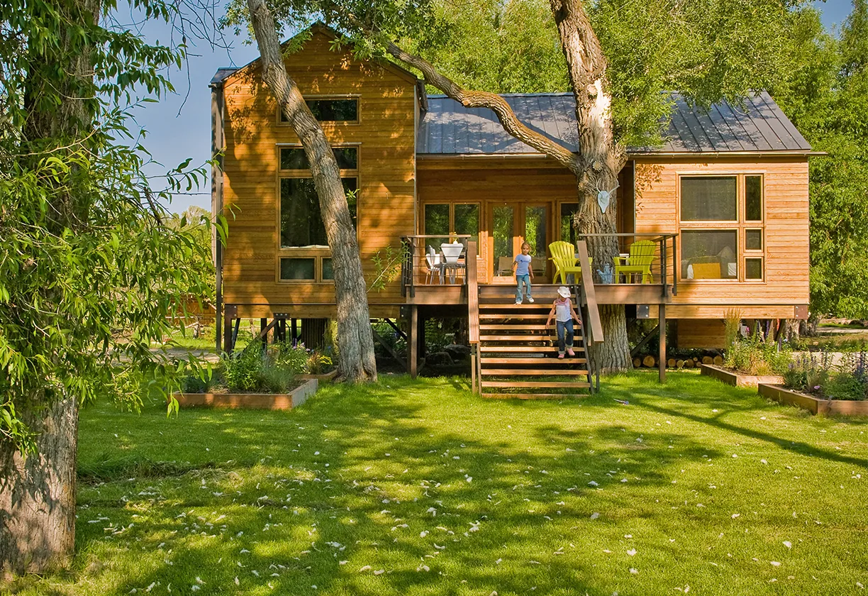 Yellowstone River Cabin features a stilt foundation, wood siding, metal roof, and a deck with metal railing and outdoor dining seating.