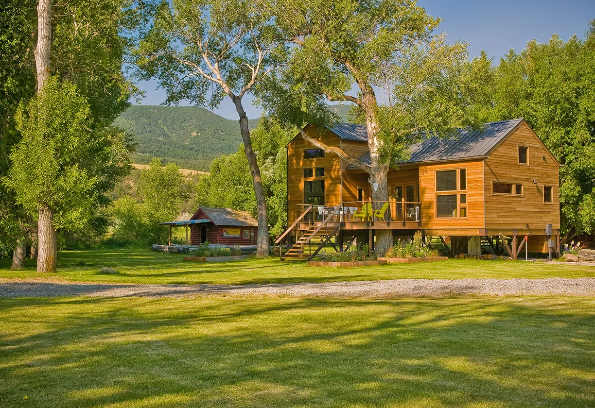 The Yellowstone River Cabin features wood siding and a metal roof elevated on stilts with an outside deck and metal railing.