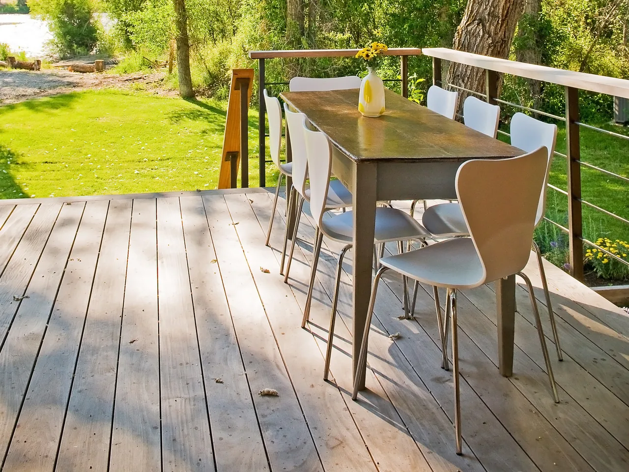 Dining area on the outdoor deck with a wooden table and white chairs surrounded by a railing.