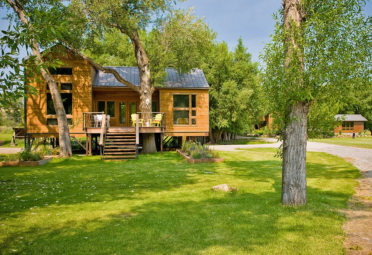 Yellowstone River Cabin by Studio Ryker features a stilt foundation with a metal roof and wooden exterior amidst lush greenery.