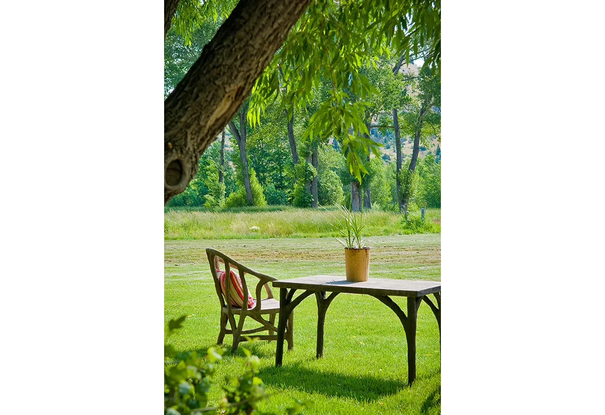 Outdoor seating area with a wooden table and chair on a grassy lawn at Yellowstone River Cabin.