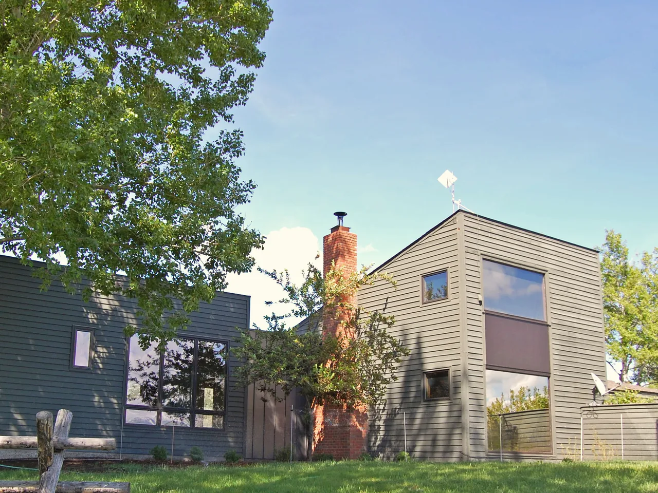 The Spring Creek Residence features modern horizontal wood siding and a prominent brick chimney between two volumes.