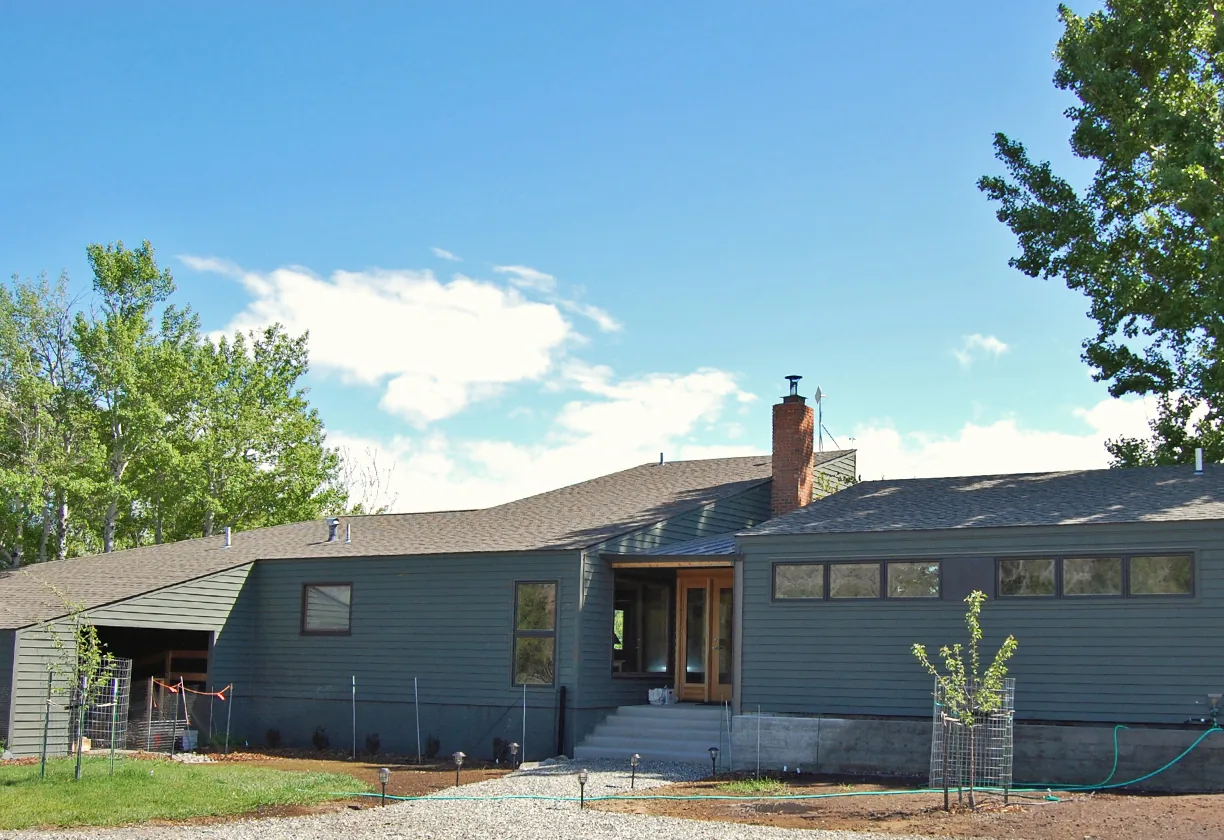 Spring Creek Residence exterior front view with large rectangular windows and weather vane visible on chimney.
