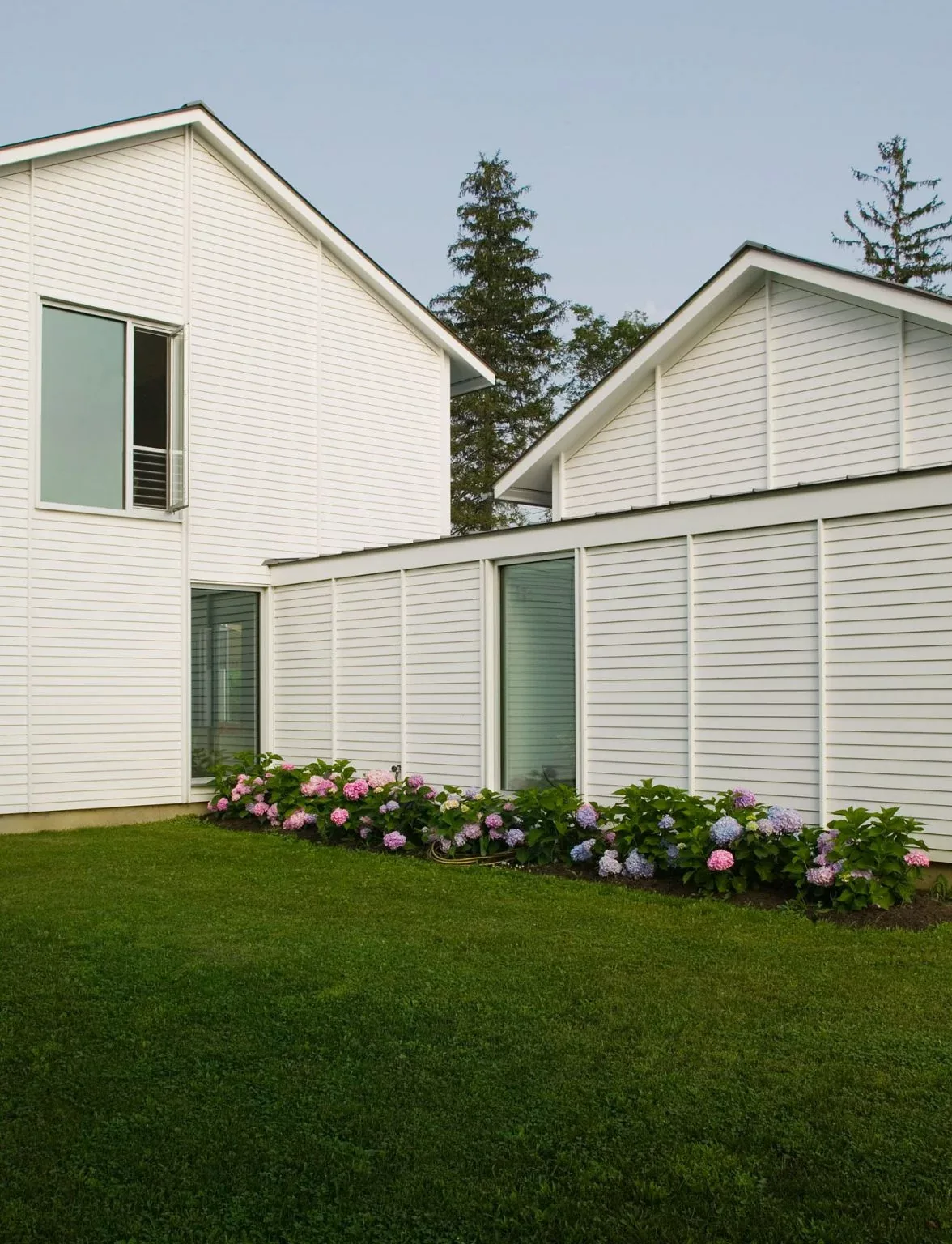 White-painted wood siding exterior with gable roof and flower bed in the yard.