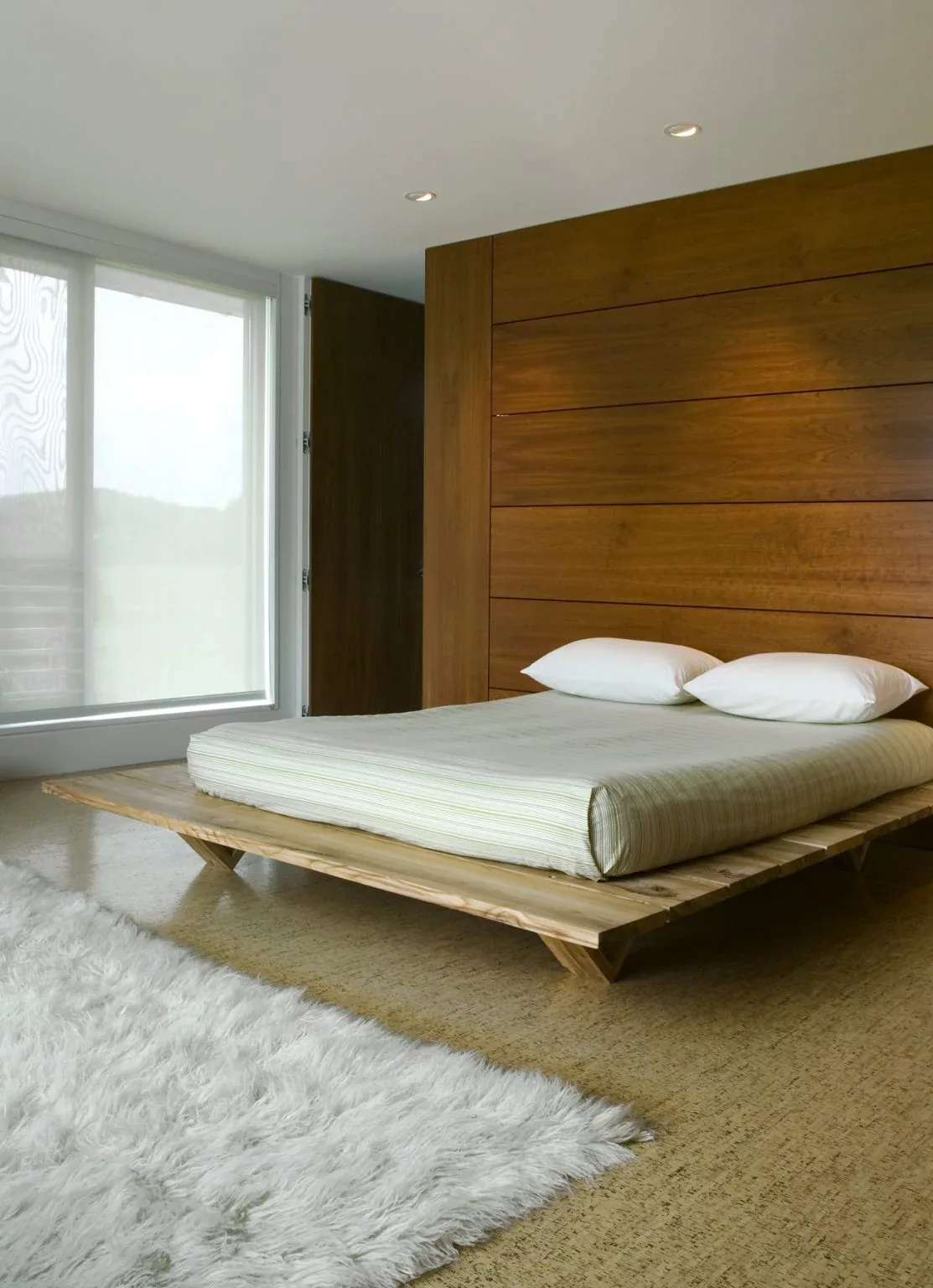 A minimalist bedroom featuring a low platform wooden bed and a wall with horizontal wood paneling.