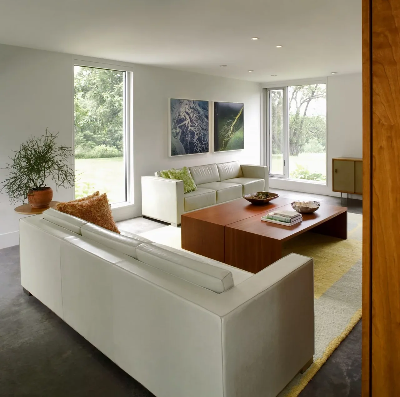 Modern living room features white leather sofas with large windows and a wooden coffee table on a yellow rug.