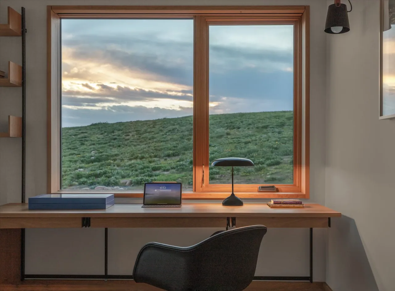 Workspace with natural wood desk and framed window overlooking hillside at sunset.
