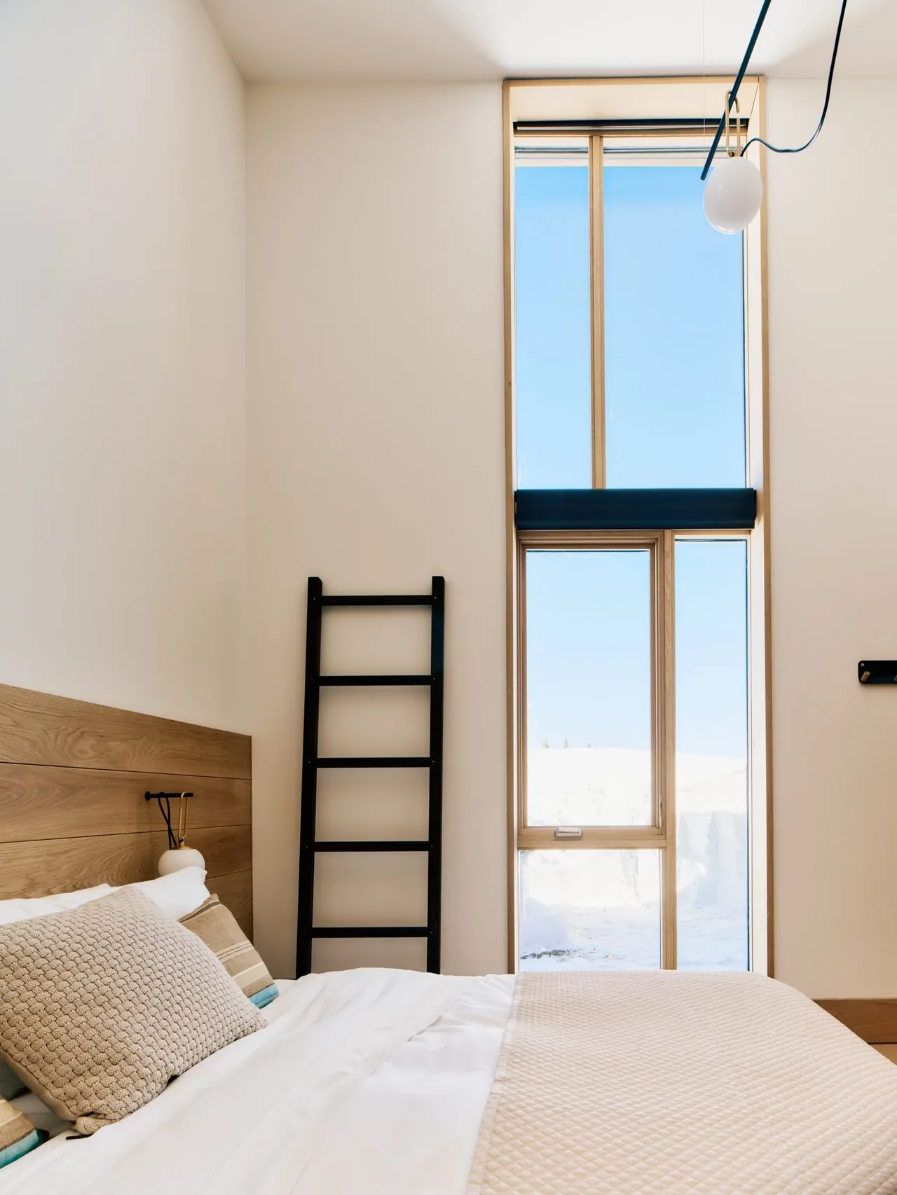 Bedroom in Overlook Cabin with a large vertical window and wood-paneled headboard, designed by studio ma.
